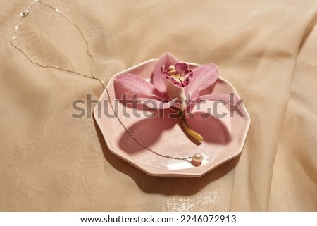 Beautiful precious chainlet and pink flower on plate on silk cloth background. Stylish glamour elegant and luxury jewelry. Studio shoot. Nobody. E-commerce. Copy space