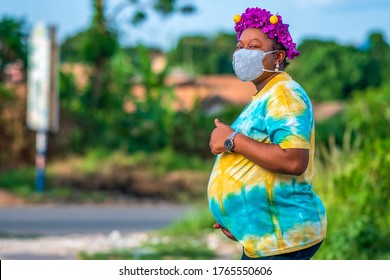 Beautiful pregnant African mother or woman wearing face mask for protection and holding abdomen-concept on obstetrics in covid-19 pandemic