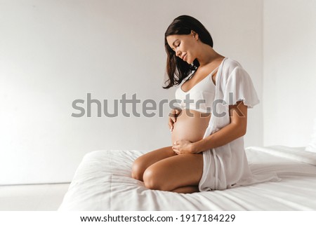 Beautiful pregnant dark-haired girl sitting on the bed