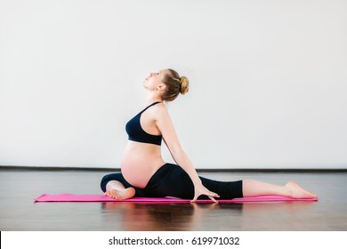 Beautiful pregnant girl doing yoga exercises in fitness studio. White background.
