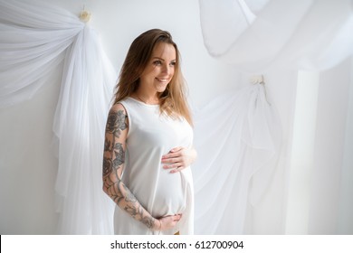 Beautiful pregnant girl with tattoo in white dress.