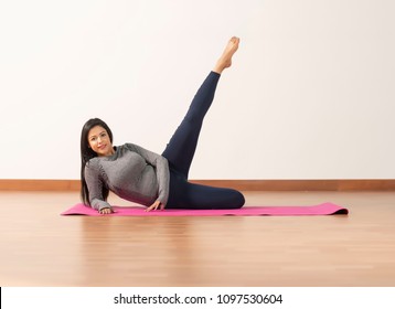 Beautiful Pregnant With Long Black Hair  Wearing Black And Gray Exercise Clothing Laying On Her Side With A Leg Lift N A Studio As She Exercise 