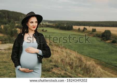 beautiful pregnant woman in black hat posing on the background of nature. pregnancy, motherhood and family concept. . High quality photo