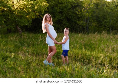 Beautiful Pregnant Woman With Curvy Hair And Eight-year-old Boy Holding Hands Outdoors