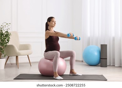 Beautiful pregnant woman with dumbbells doing exercises on fitball at home - Powered by Shutterstock