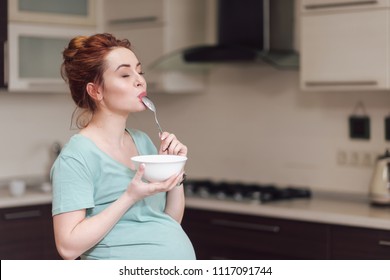 Beautiful pregnant woman eating with lust cereals on breakfast, enjoying meal. Yummy food for pregnant ladies
