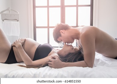 Beautiful pregnant woman and her handsome husband are kissing while spending time together in bed.