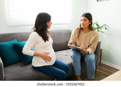Beautiful pregnant woman hired the services of a doula for her childbirth. Pretty midwife asking questions about her pregnancy to a caucasian woman at home