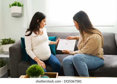 Beautiful pregnant woman and latin midwife holding a calendar. Doula and expectant mother talking about the due date while sitting on the couch