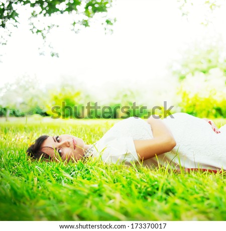 Beautiful Pregnant Woman lies on the Grass in sunlight and touching her belly, outdoor, pregnancy as natural process