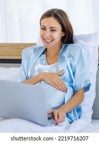 Beautiful Pregnant Woman  Pajamas Resting On Bed With Smile And Happy To Watch Laptop For Prenatal Care Of Maternity. Healthy Mom Relax And Pleased With Belly Of Unborn Baby For Expecting Child Birth.