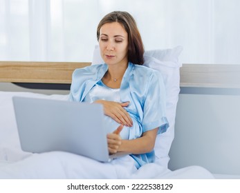 Beautiful Pregnant Woman  Pajamas Resting On Bed With Smile And Happy To Watch Laptop For Prenatal Care Of Maternity. Healthy Mom Relax And Pleased With Belly Of Unborn Baby For Expecting Child Birth.