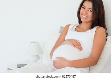 Beautiful pregnant woman posing while lying on a bed at home