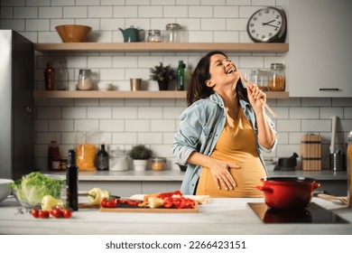 Beautiful pregnant woman preparing delicious food. Smiling woman having fun while cooking at home.	 - Powered by Shutterstock