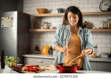 Beautiful pregnant woman preparing delicious food. Smiling woman cooking pasta at home. - Powered by Shutterstock