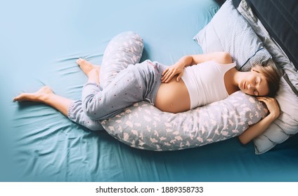 Beautiful pregnant woman relaxing or sleeping with belly support pillow in bed. Young mother waiting of a baby. Concept of pregnancy, maternity, healthcare, gynecology, medicine.
