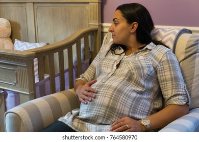 Beautiful pregnant woman sit in rocking chair next to crib touching tummy excited to wait for birth of new baby girl - Powered by Shutterstock