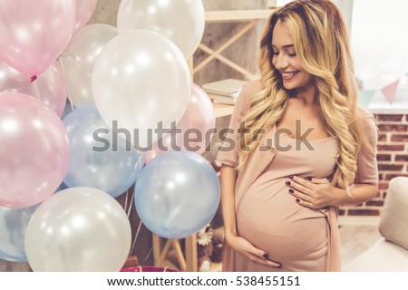 Beautiful pregnant woman is smoothing her tummy and smiling during baby shower