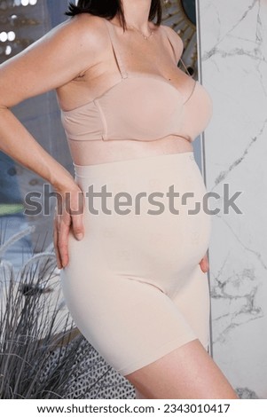 Beautiful pregnant woman in special beige pregnancy underwear. Advertisement of comfortable basic pregnancy underpants. Happy brunette girl show her panties in hall. Caucausian thin woman