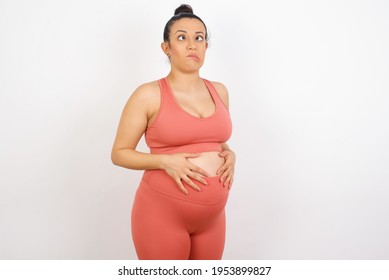 Beautiful pregnant woman in sports clothes against white background making grimace and crazy face, screaming out of control, funny lunatic expressing freedom and wild.