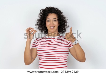 Beautiful pregnant woman standing over white studio background holding an invisible braces aligner and rising thumb up, recommending this new treatment. Dental healthcare concept.