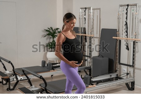 Beautiful pregnant woman stands in a yoga studio and gently touches her belly. 