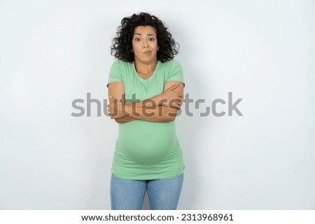 Beautiful pregnant woman wearing green T-shirt standing over white studio background shaking and freezing for winter cold with sad and shock expression on face.