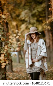 Beautiful pregnant woman wearing poncho and hat in park