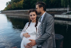 Beautiful Pregnant Woman In White Dress With Handsome Man Standing On A Wooden Pier Against Lake