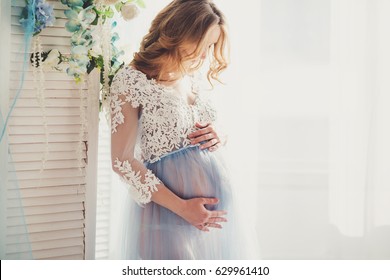 Beautiful pregnant young woman is wearing luxury blue lingerie dress at home
