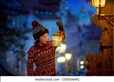 Beautiful preschool child, holding lantern, casually dressed, looking at night view of Prague city, wintertime