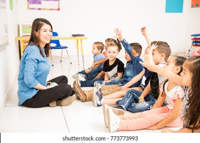 Beautiful Preschool Teacher And Her Group Of Students Raising Their Hands And Having Some Fun At School