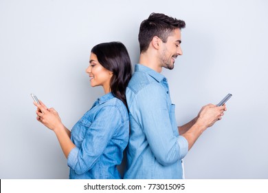 Beautiful, pretty, cute woman and handsome man in jeans shirts standing back to back and writing sms through 3g internet on smart phones over grey background - Powered by Shutterstock