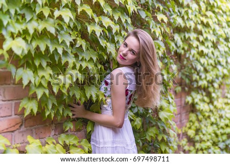Beautiful pretty girl against background of brick wall with green leaves