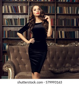 Beautiful Pretty Girl In Black Sheath Cocktail Dress Posing In Luxury Library Interior. Young Female Model Fashion Portrait