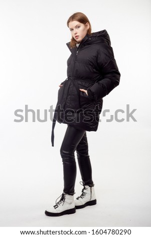 Beautiful   pretty girl with long brown hair and perfect body weared in black leather pants and gray sweater, down jacket, white boots. Isolated on white background.