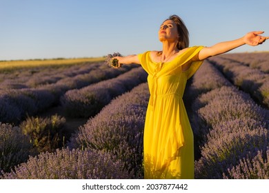 Beautiful and pretty young woman in a yellow dress relaxes and enjoys a walk in the lavender field at sunset, toned