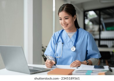 A beautiful and professional Asian female doctor is working on her medical cases on her laptop or making a video call medical consultation with a patient while sitting in her office. - Powered by Shutterstock