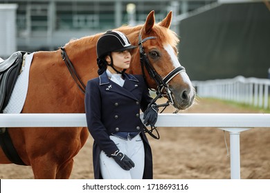 Beautiful professional female jockey standing near horse. woman horse rider is preparing to equitation. girl and horse. equestrian sport concept. dressage horse  - Powered by Shutterstock