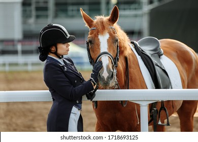 Beautiful Professional Female Jockey Standing Near Horse. Woman Horse Rider Is Preparing To Equitation. Girl And Horse. Equestrian Sport Concept. Dressage Horse 