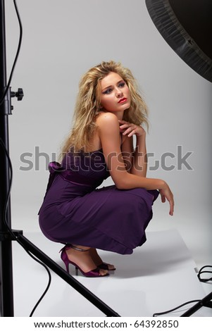 beautiful professional female model in purple dress resting between shots in a photographic studio shoot set-up