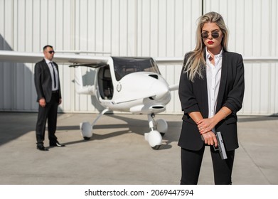 Beautiful Professional Female Spy Agent Bodyguard With Gun Securing Airplane On Private Airport. Security Police Woman In Civilian Black Suit. Close Security Protection