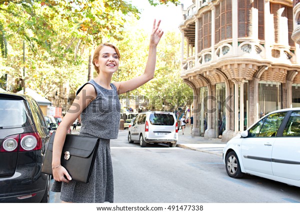 Beautiful professional woman calling a taxi in a\
classic street, smiling on a sunny day, outdoors road with traffic\
and stone buildings. Business woman in a rush, hitching a cab in\
financial city.