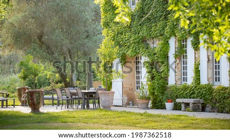 Beautiful Provencal farmhouse in the Camargue countryside. Virginia creeper on the facade, white shutters and a welcoming table on the terrace in front of the house. Golden light on a June evening