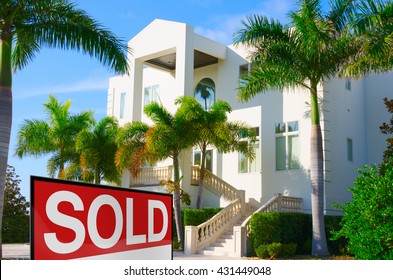 Beautiful Purchased Luxury Residential Home With Front Stairways And Lush Green Palm Trees Against A Blue Morning Sky With A Bright SOLD Sign In The Front Yard.