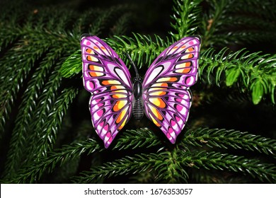 Beautiful Purple Butterfly Figurine Decoration On Real Natural Christmas Tree Plant. Close Up Of Purple Fake Butterfly Three Dimensional Stick For Interior Decorations Or Lawn Decor DIY