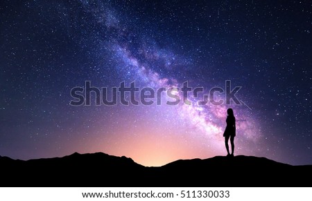 Beautiful purple Milky Way with standing woman. Colorful landscape with night sky with stars and silhouette of a girl on mountain on the background of beautiful galaxy. Milky way with yellow light.