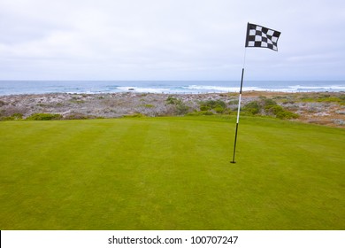 Beautiful Putting Green And Pin Flag Fluttering In The Ocean Breeze On A Scenic, Golf Course Situated On The Pacific Ocean. Dramatic Cloudy Sky Overhead.