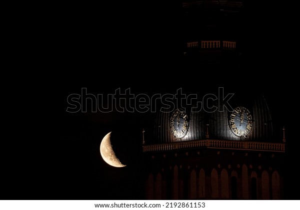 Beautiful quarter moon over Riga\
old town behind Domes cathedral clock. Night sky with amazing\
moon.
