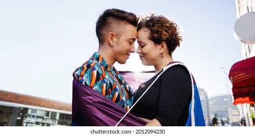 Beautiful queer couple bonding outdoors. Young LGBTQ couple standing together with a rainbow pride flag around them. Two non-conforming lovers touching their foreheads together affectionately. - Powered by Shutterstock